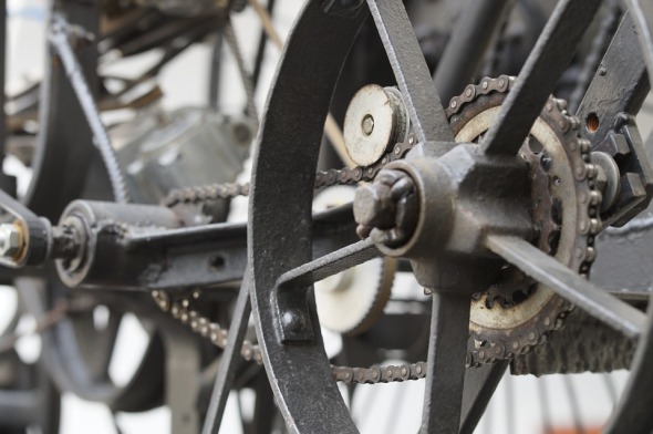 Some cast-iron wheels and gears, connected with a bicycle chain.
